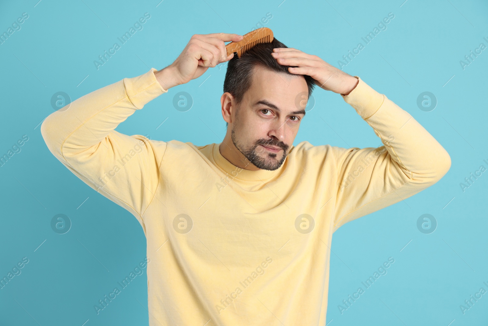 Photo of Handsome man stylish his hair with comb on light blue background