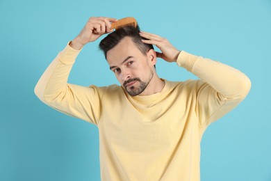 Photo of Handsome man stylish his hair with comb on light blue background