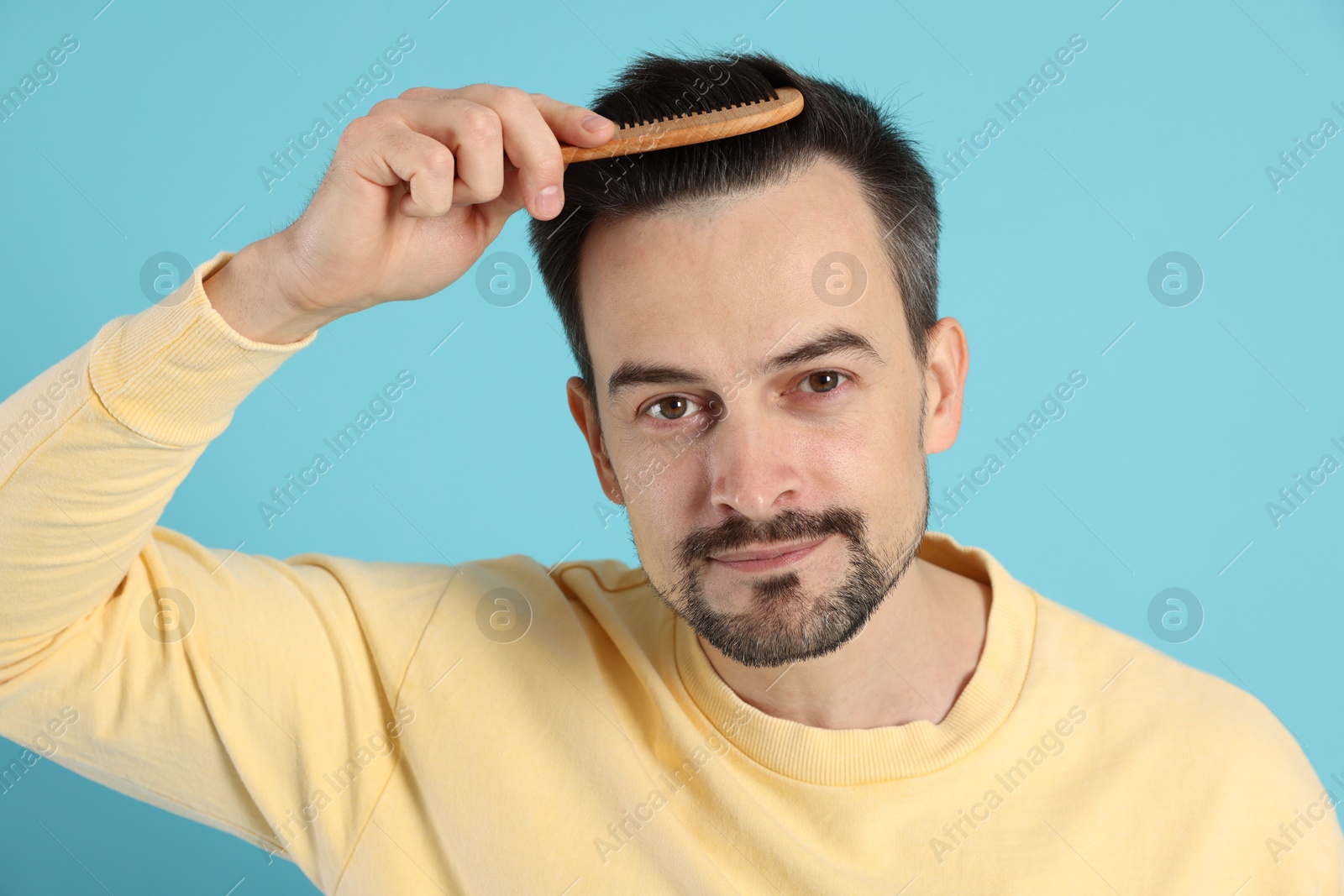 Photo of Handsome man stylish his hair with comb on light blue background