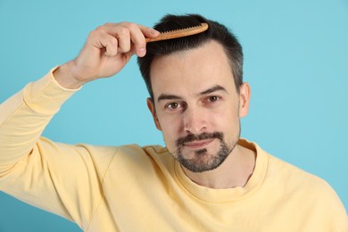 Photo of Handsome man stylish his hair with comb on light blue background