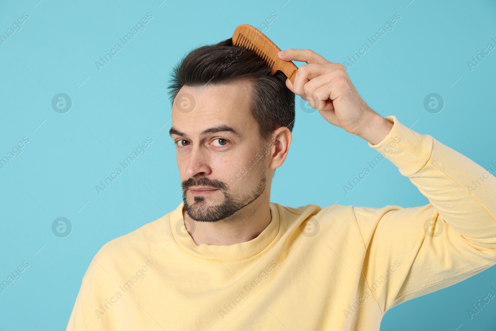 Photo of Handsome man stylish his hair with comb on light blue background