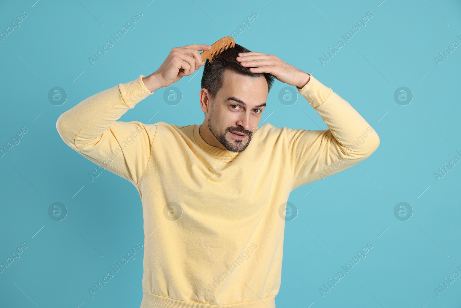 Photo of Handsome man stylish his hair with comb on light blue background