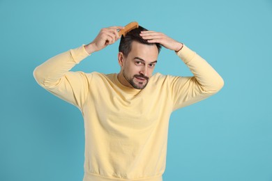 Photo of Handsome man stylish his hair with comb on light blue background