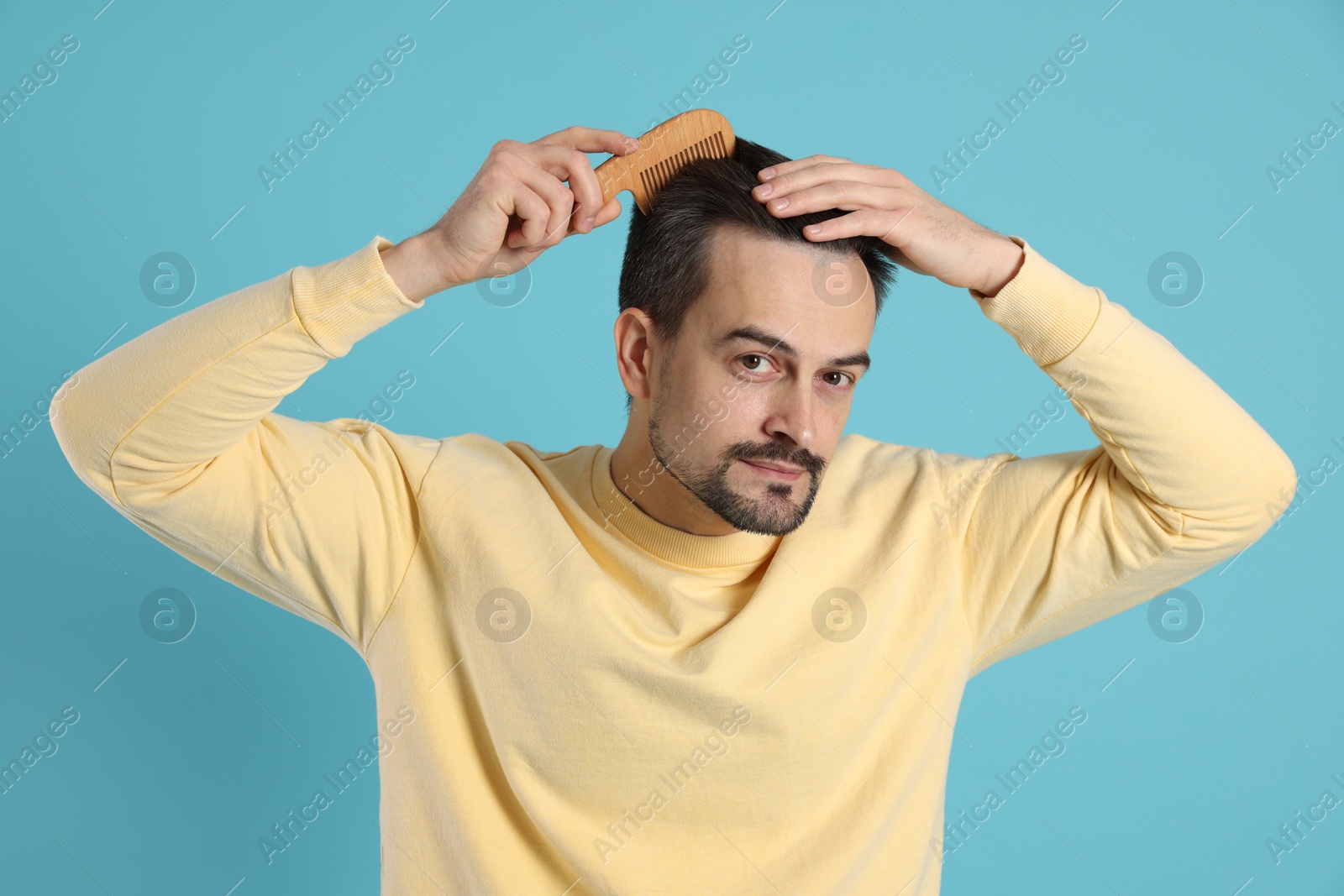 Photo of Handsome man stylish his hair with comb on light blue background