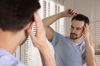 Photo of Handsome man styling his hair with comb near mirror at home