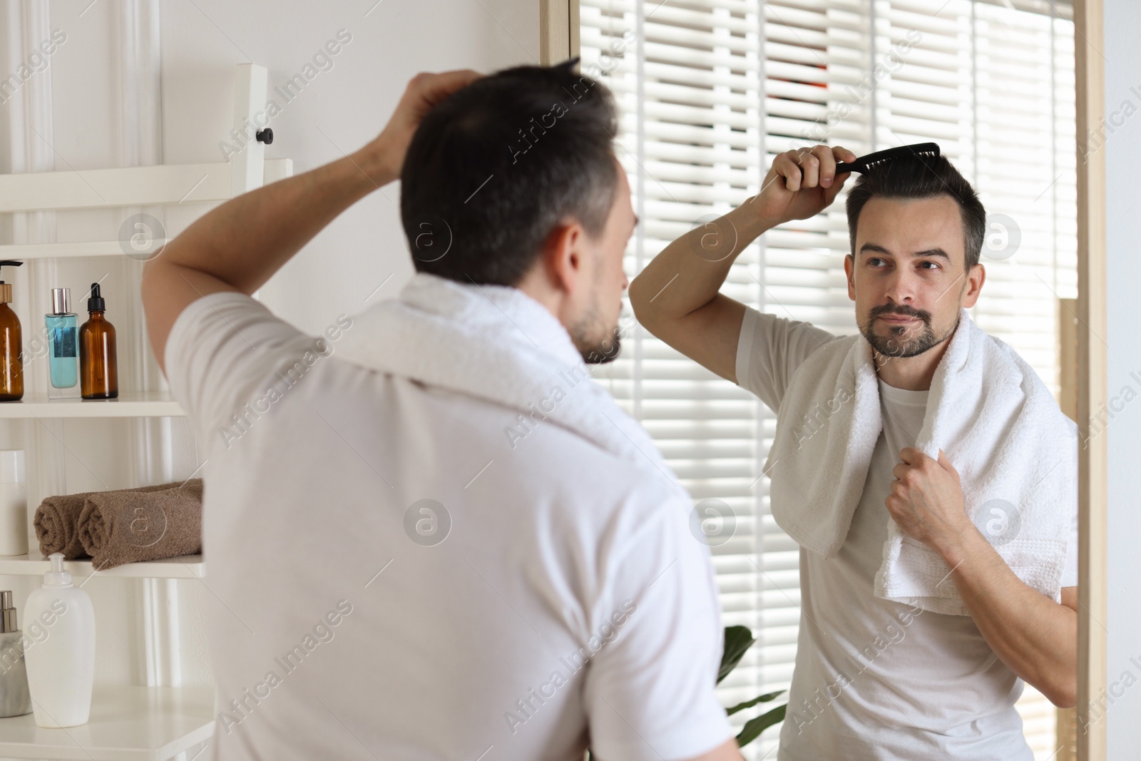 Photo of Handsome man styling his hair with comb near mirror at home