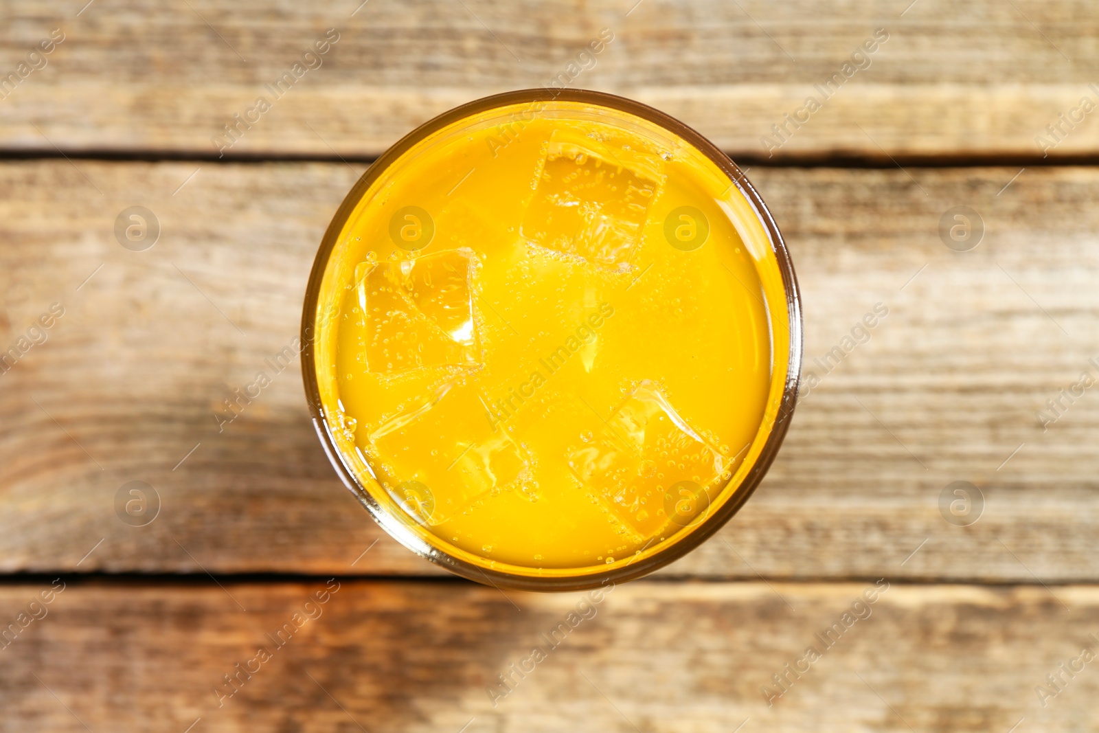 Photo of Sweet soda water with ice cubes in glass on wooden table, top view