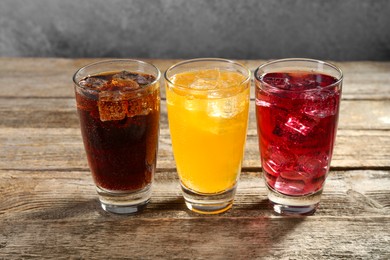 Photo of Soda water of different flavors with ice cubes in glasses on wooden table