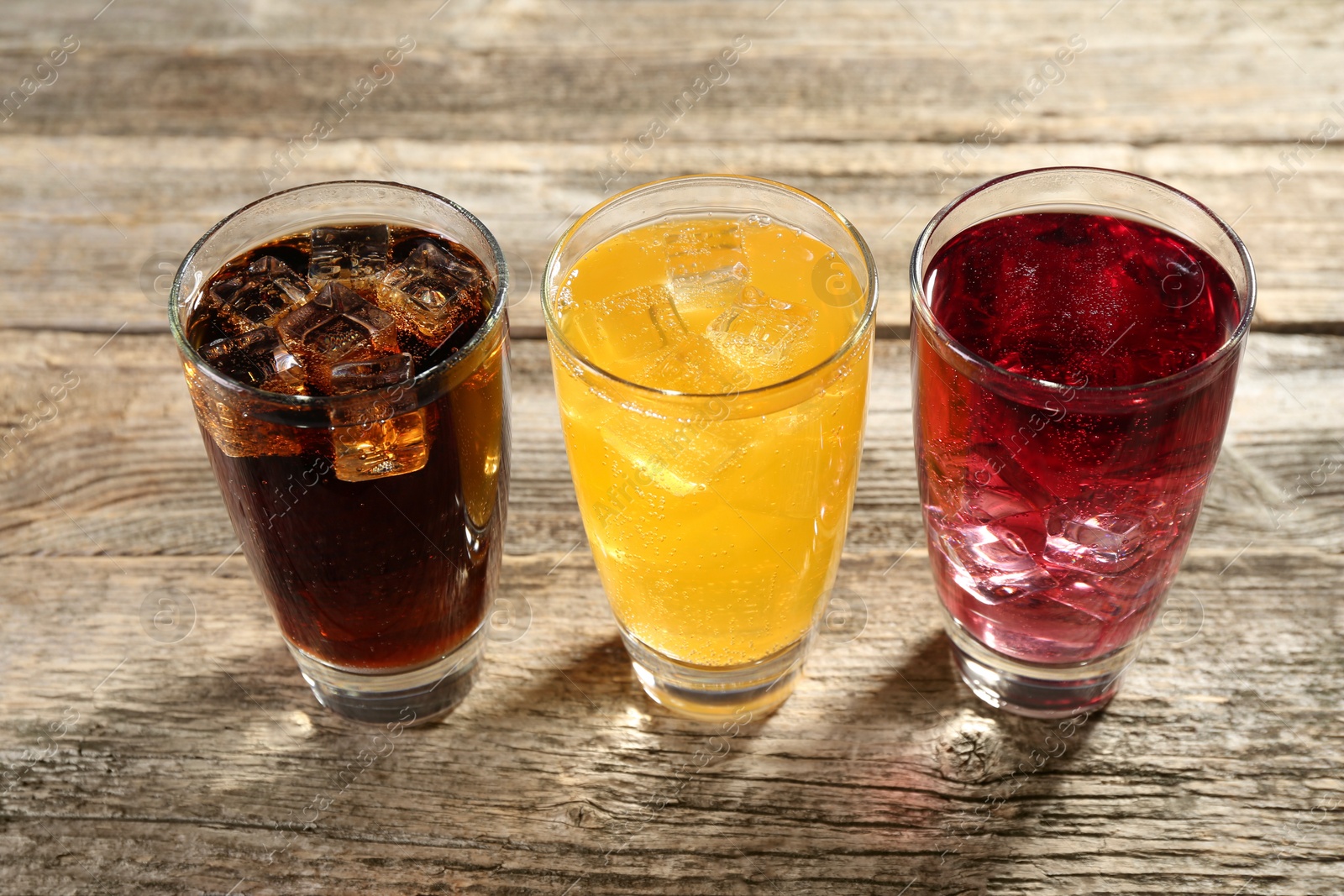 Photo of Soda water of different flavors with ice cubes in glasses on wooden table, closeup