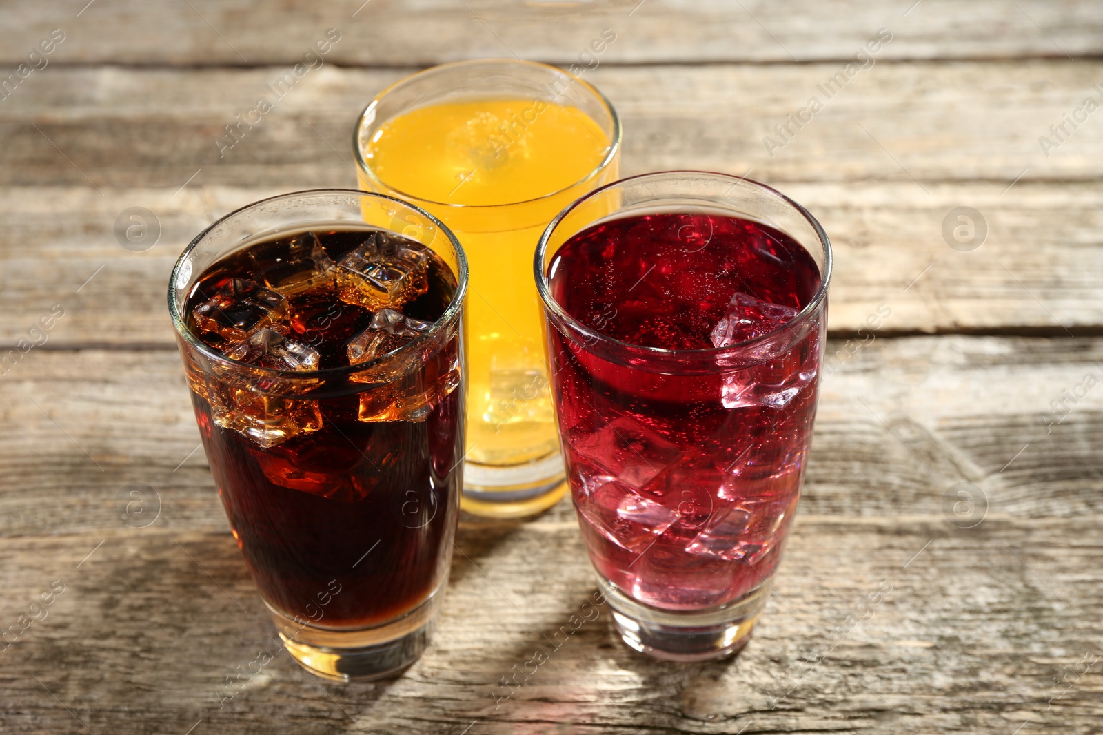 Photo of Soda water of different flavors with ice cubes in glasses on wooden table, closeup