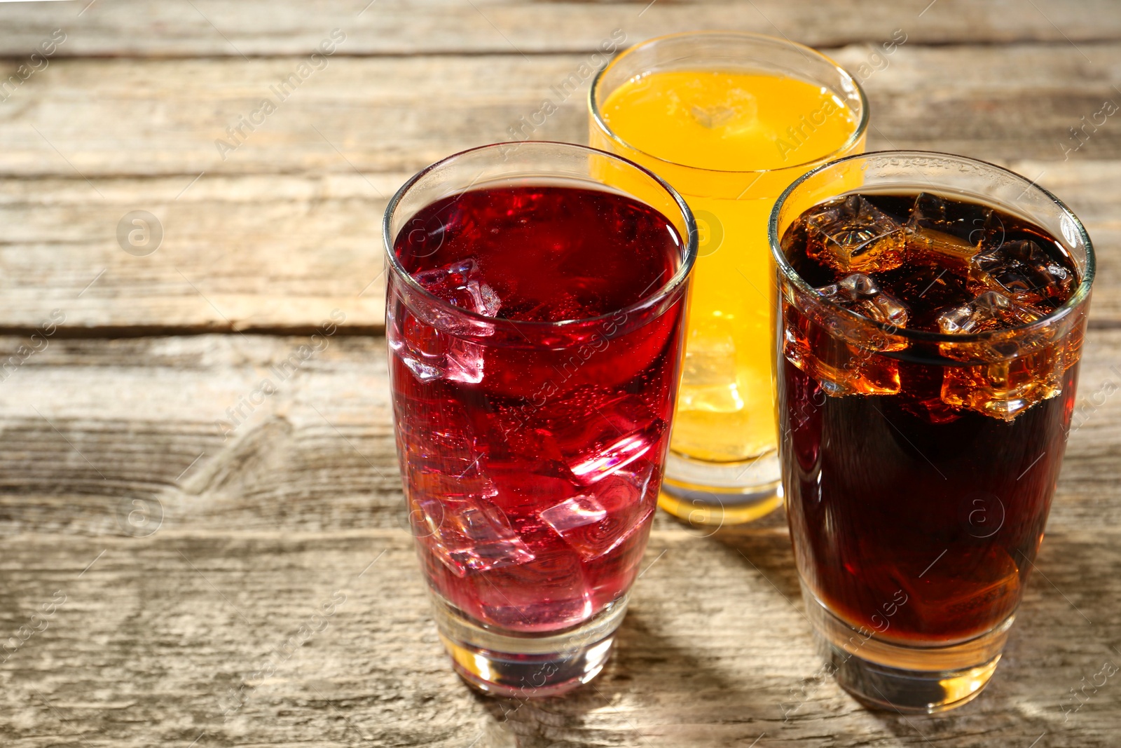 Photo of Soda water of different flavors with ice cubes in glasses on wooden table, closeup. Space for text