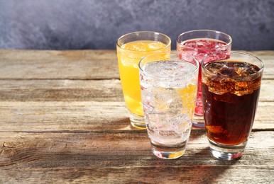 Photo of Soda water of different flavors with ice cubes in glasses on wooden table, space for text