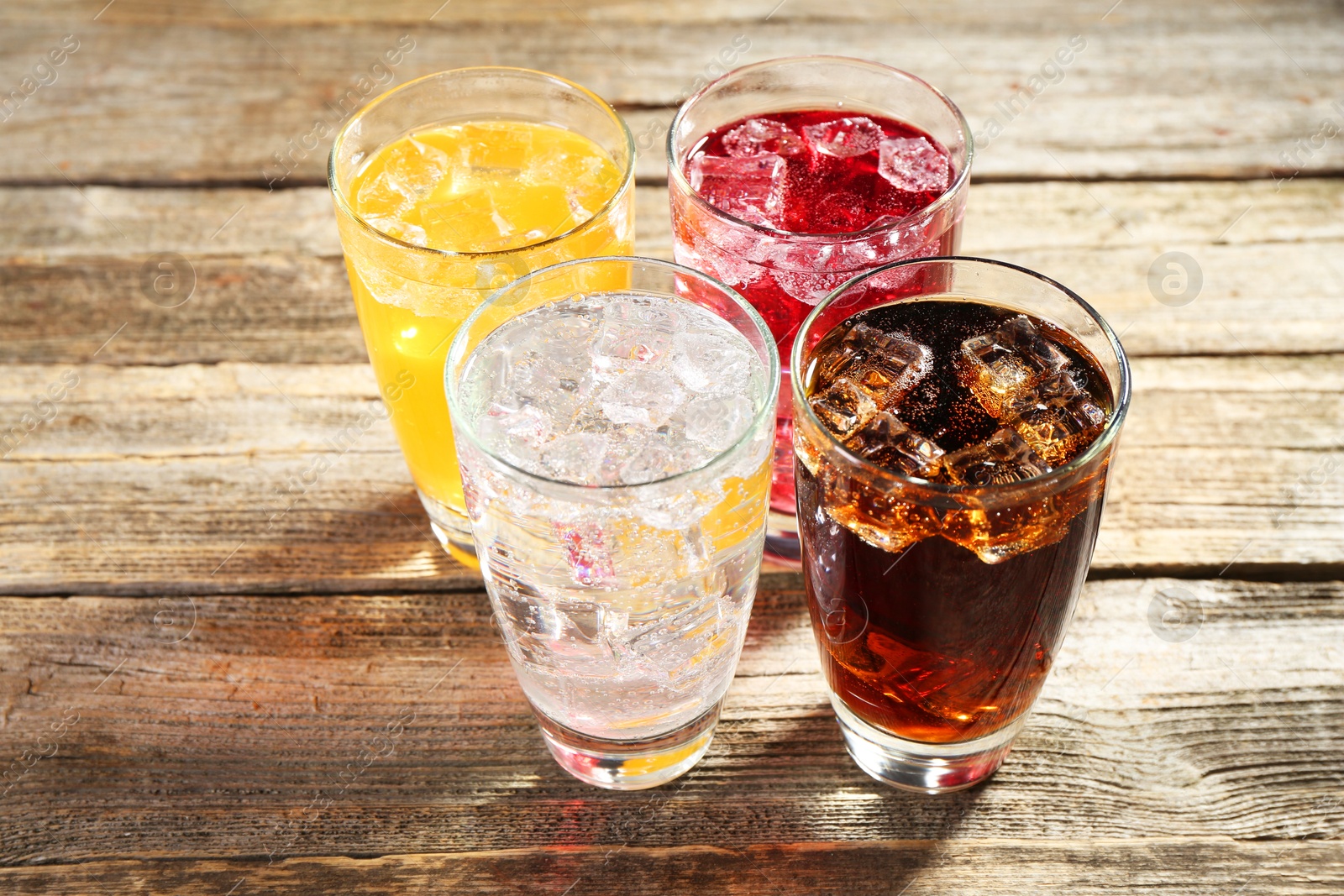 Photo of Soda water of different flavors with ice cubes in glasses on wooden table, closeup