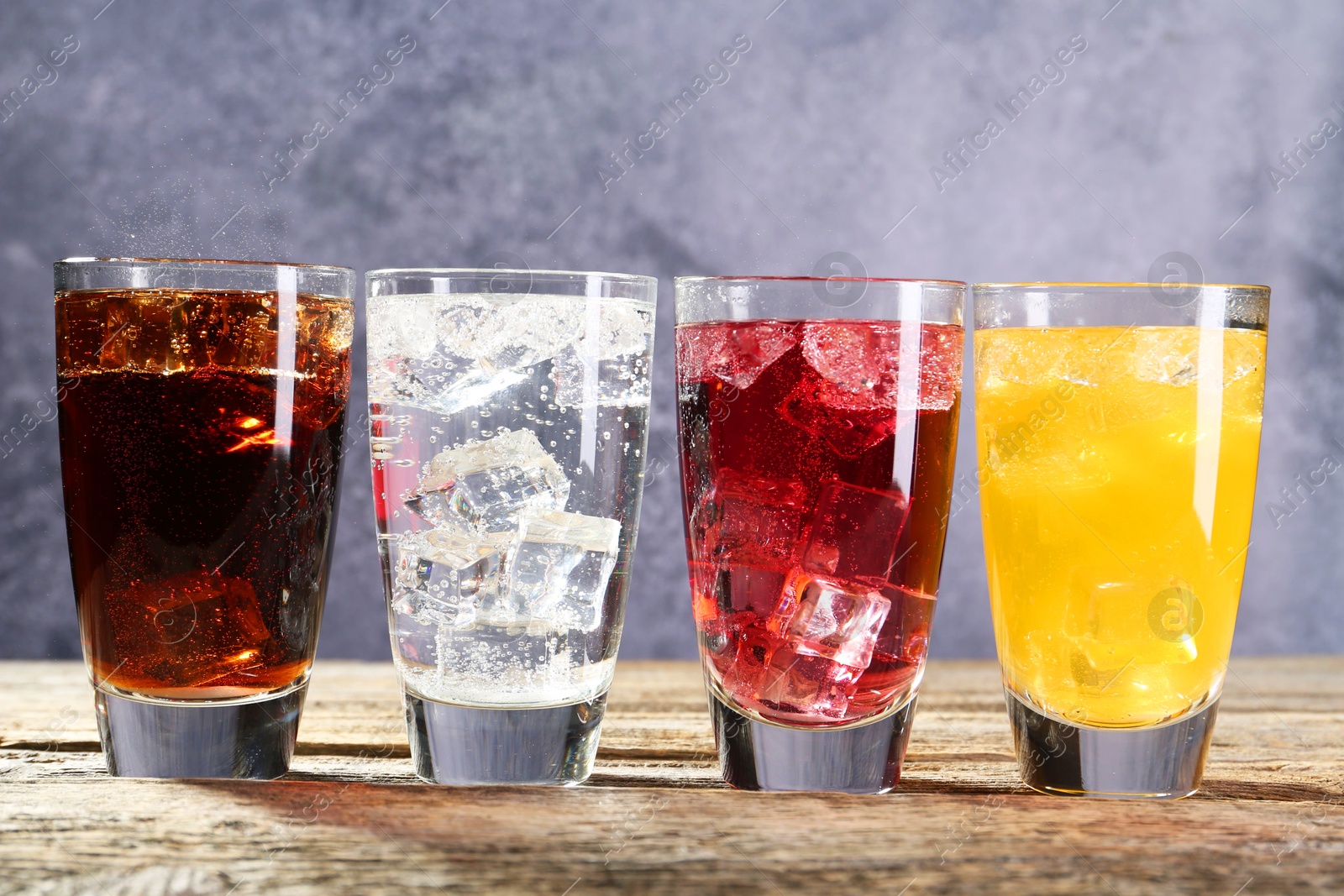 Photo of Soda water of different flavors with ice cubes in glasses on wooden table