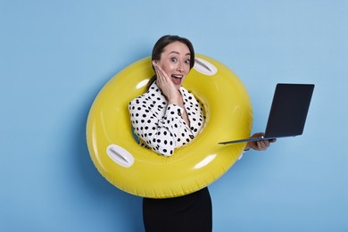 Photo of Surprised businesswoman with inflatable ring and laptop on light blue background