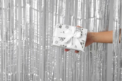 Photo of Man with gift box near silver foil curtain against light background, closeup. Space for text