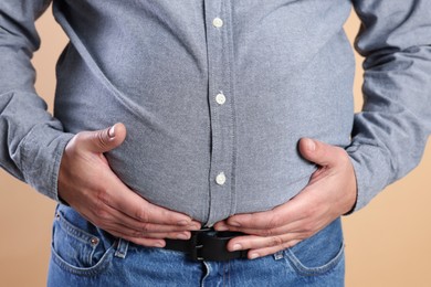 Photo of Overweight man in tight shirt on beige background, closeup