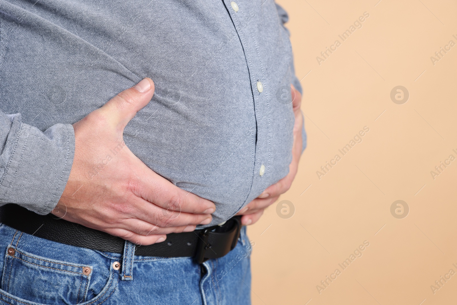 Photo of Overweight man in tight shirt on beige background, closeup. Space for text