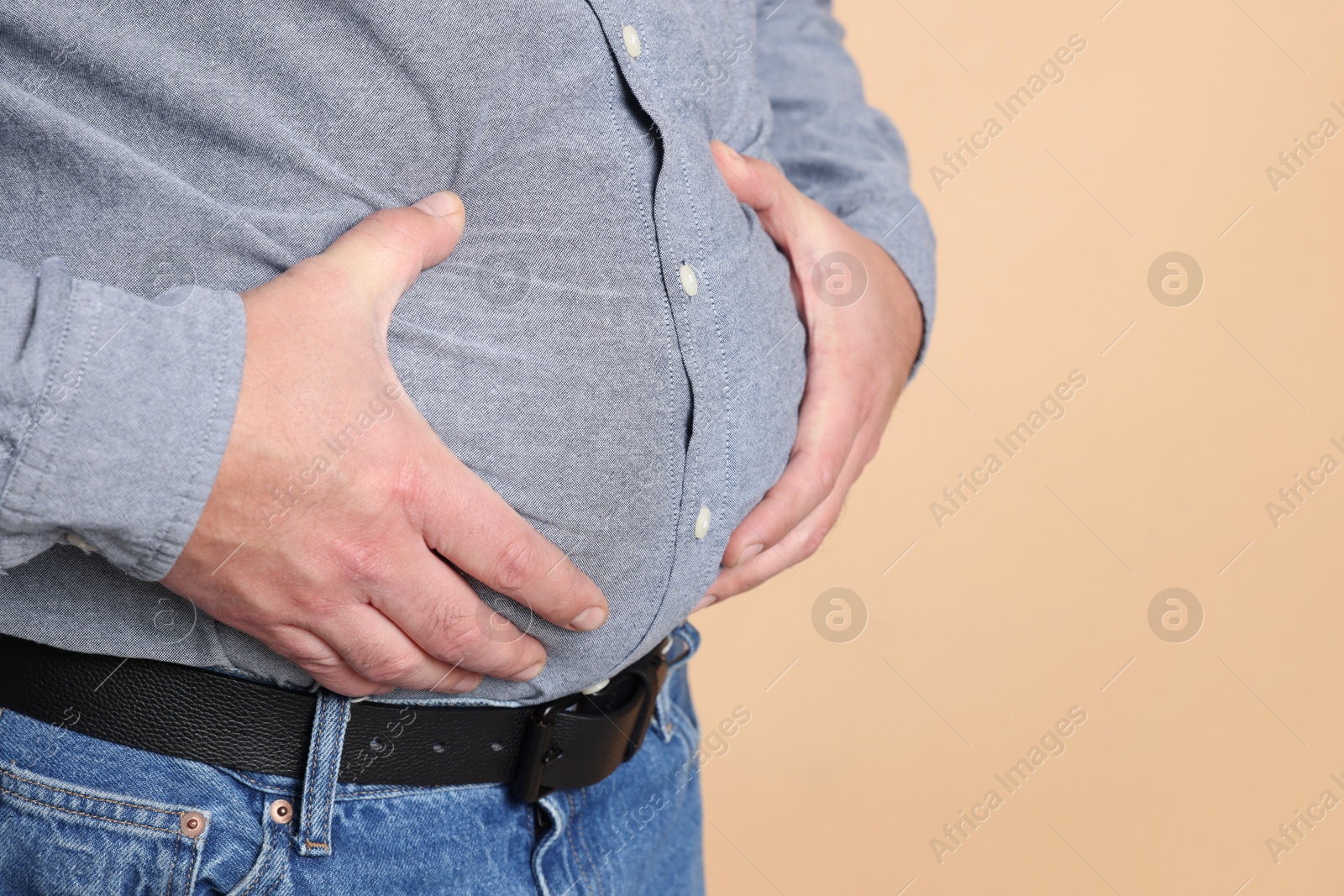 Photo of Overweight man in tight shirt on beige background, closeup. Space for text