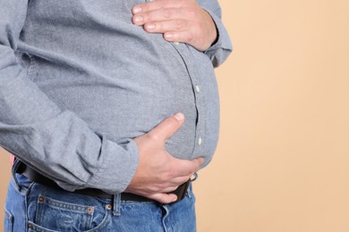 Photo of Overweight man in tight shirt on beige background, closeup. Space for text