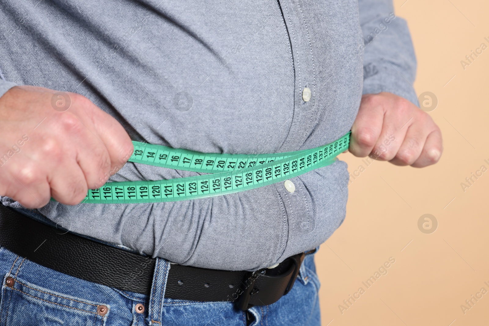 Photo of Overweight man measuring his belly with tape on beige background, closeup