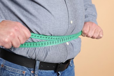 Photo of Overweight man measuring his belly with tape on beige background, closeup