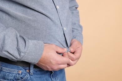 Photo of Overweight man trying to button up tight shirt on beige background, closeup. Space for text