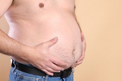 Photo of Overweight problem. Man with excessive belly fat on beige background, closeup. Space for text