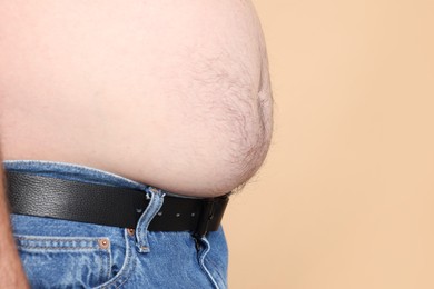 Photo of Overweight problem. Man with excessive belly fat on beige background, closeup. Space for text