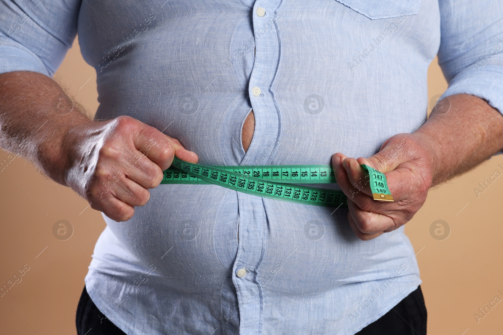 Photo of Overweight man measuring his belly with tape on beige background, closeup