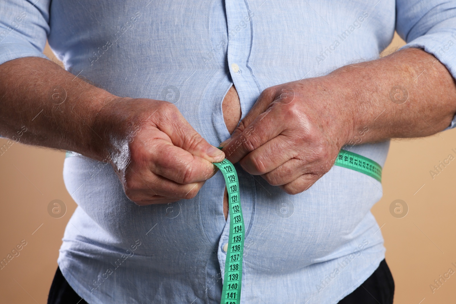 Photo of Overweight man measuring his belly with tape on beige background, closeup