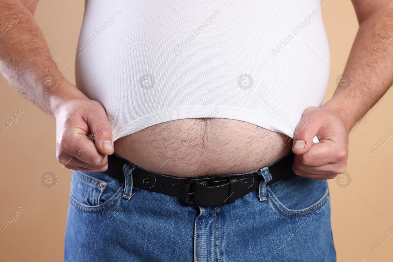 Photo of Overweight man in tight t-shirt on beige background, closeup