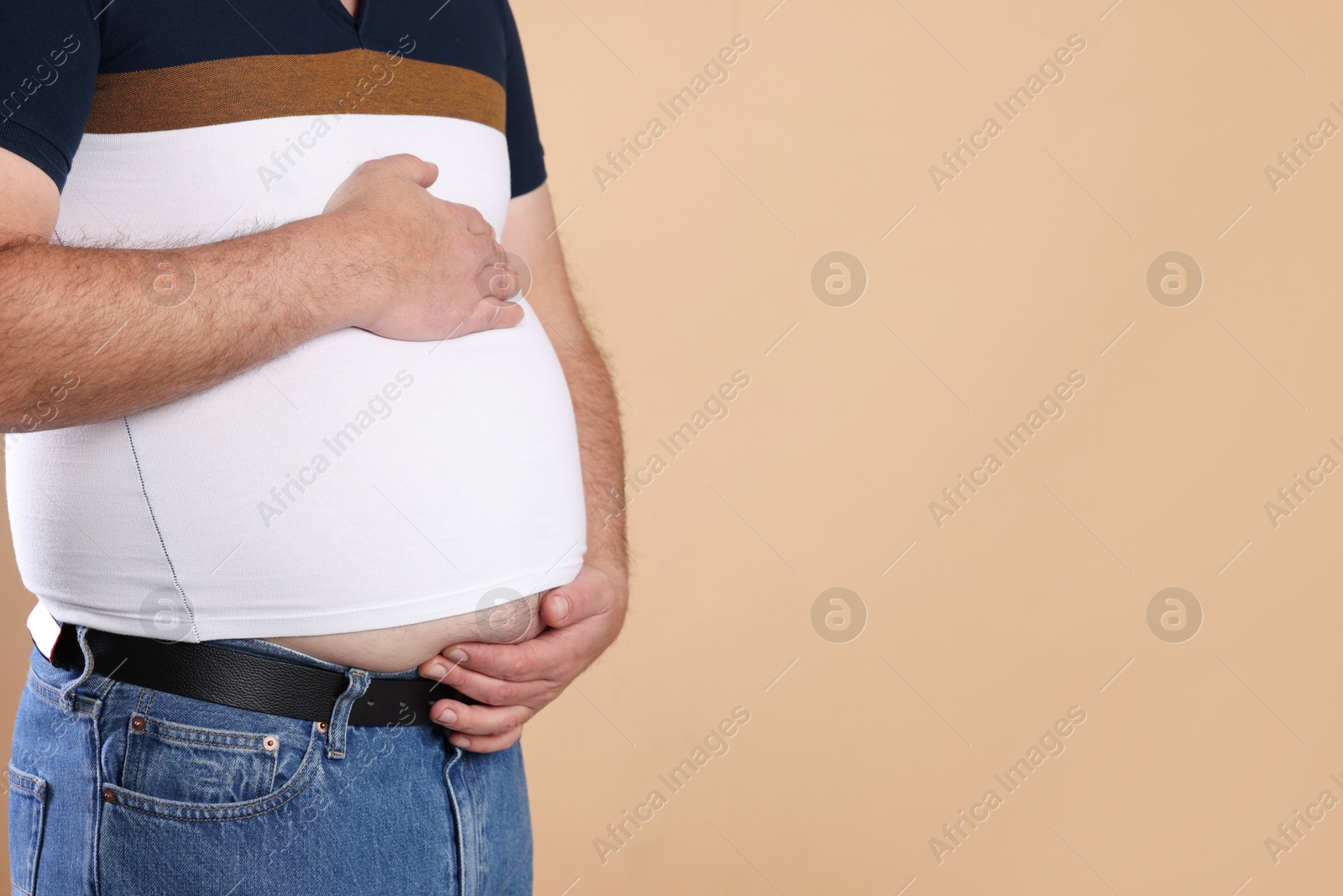 Photo of Overweight man in tight t-shirt on beige background, closeup. Space for text