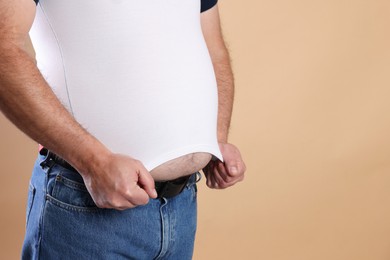 Photo of Overweight man in tight t-shirt on beige background, closeup. Space for text