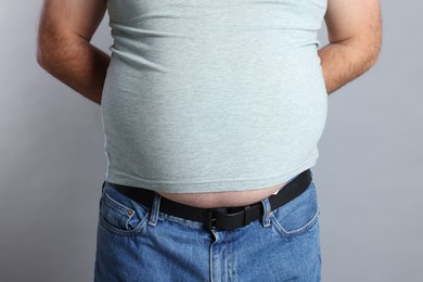 Photo of Overweight man in tight t-shirt on grey background, closeup