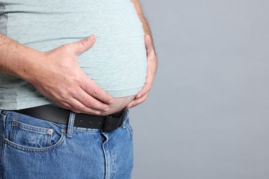 Photo of Overweight man in tight t-shirt on grey background, closeup. Space for text