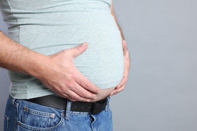 Photo of Overweight man in tight t-shirt on grey background, closeup. Space for text