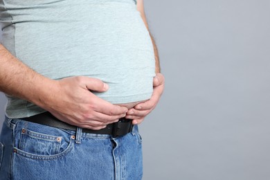 Photo of Overweight man in tight t-shirt on grey background, closeup. Space for text