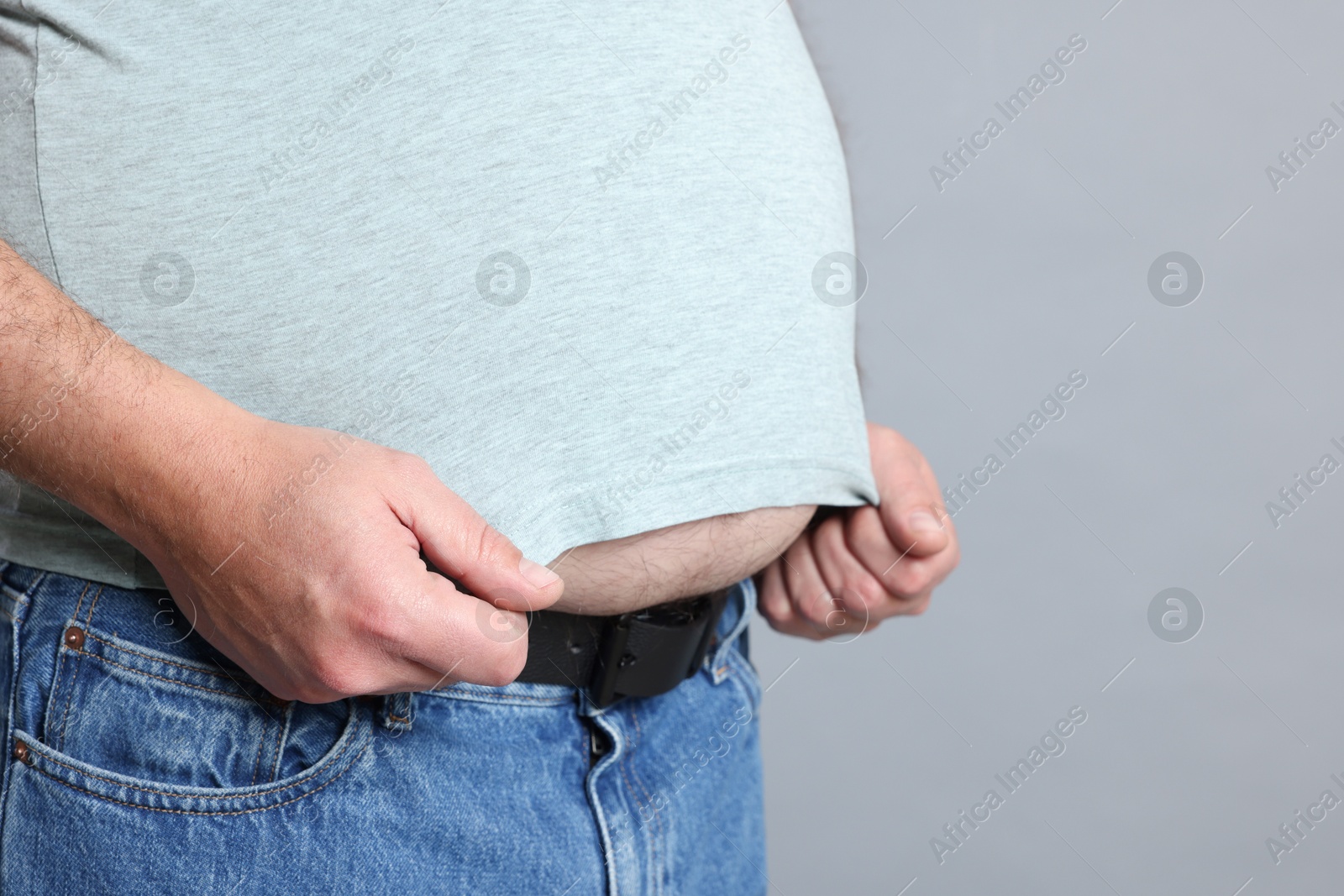 Photo of Overweight man in tight t-shirt on grey background, closeup. Space for text