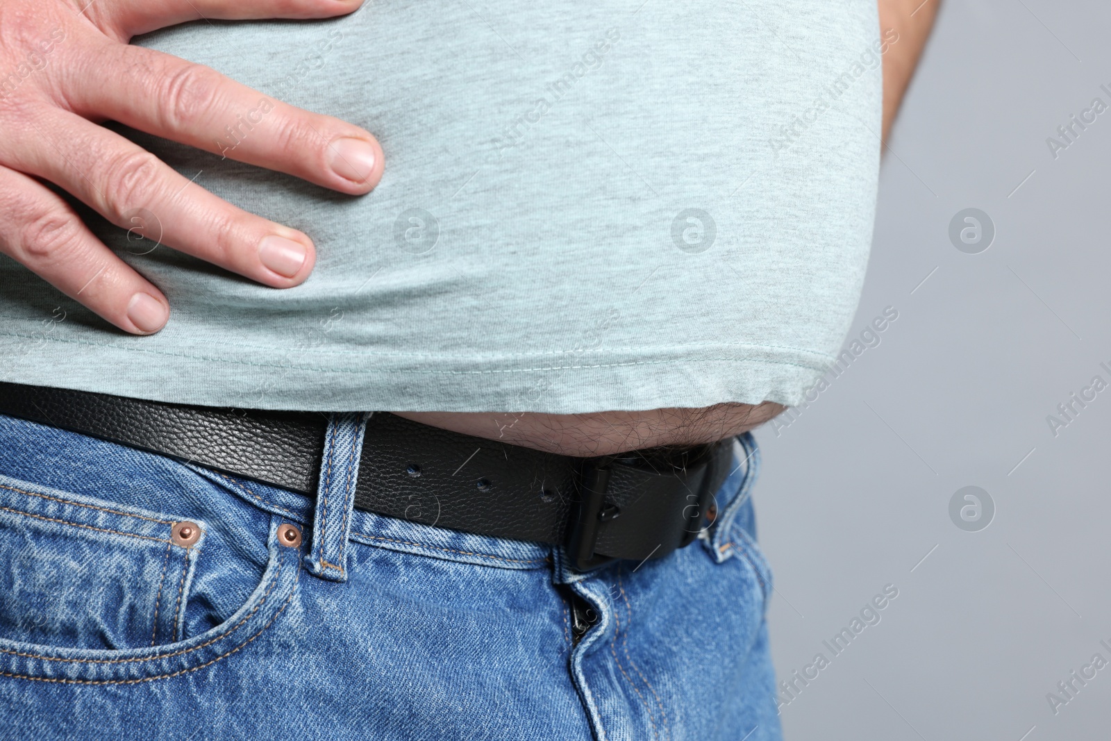 Photo of Overweight man in tight t-shirt on grey background, closeup