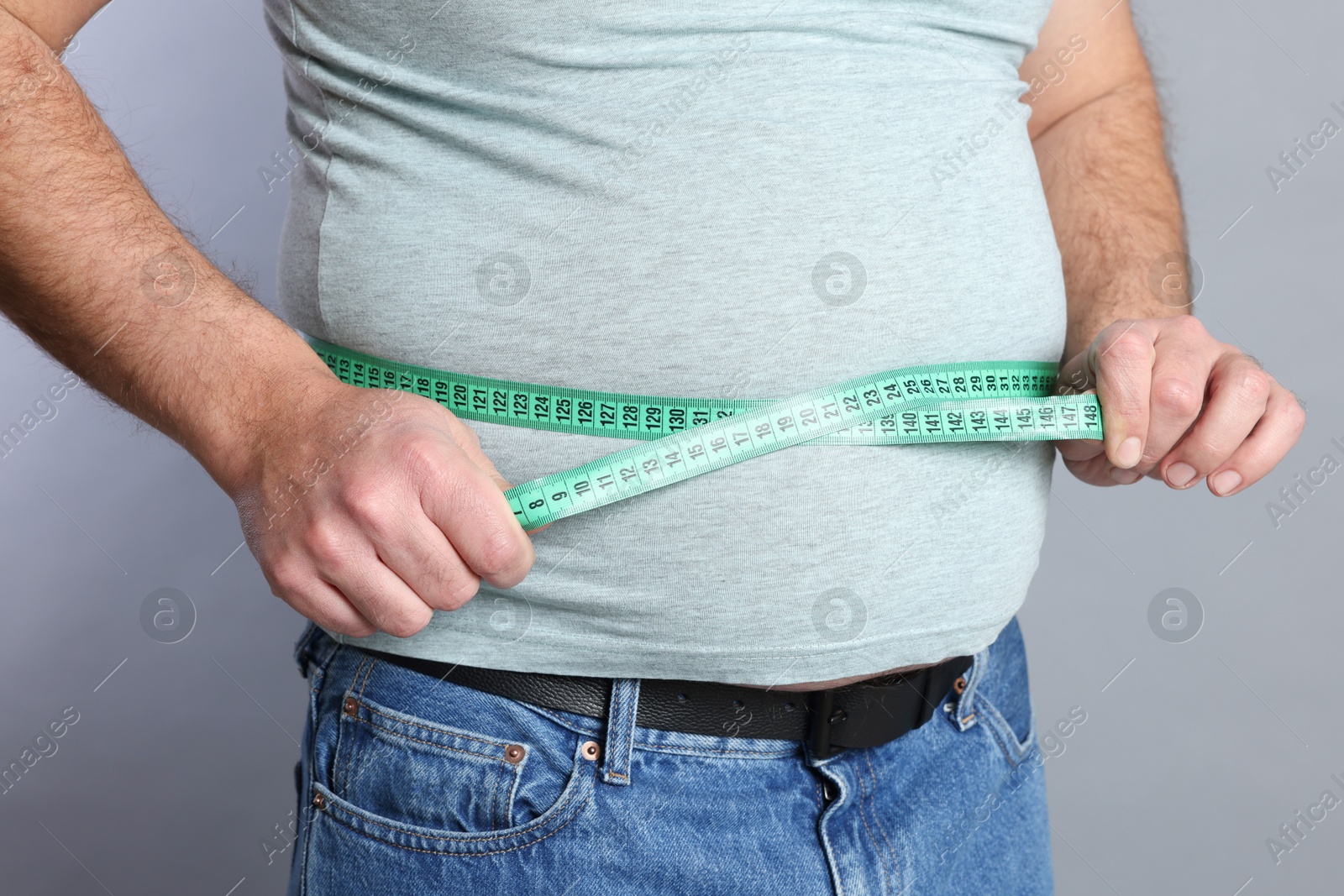 Photo of Overweight man measuring his belly with tape on grey background, closeup