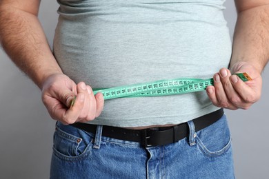 Photo of Overweight man measuring his belly with tape on grey background, closeup