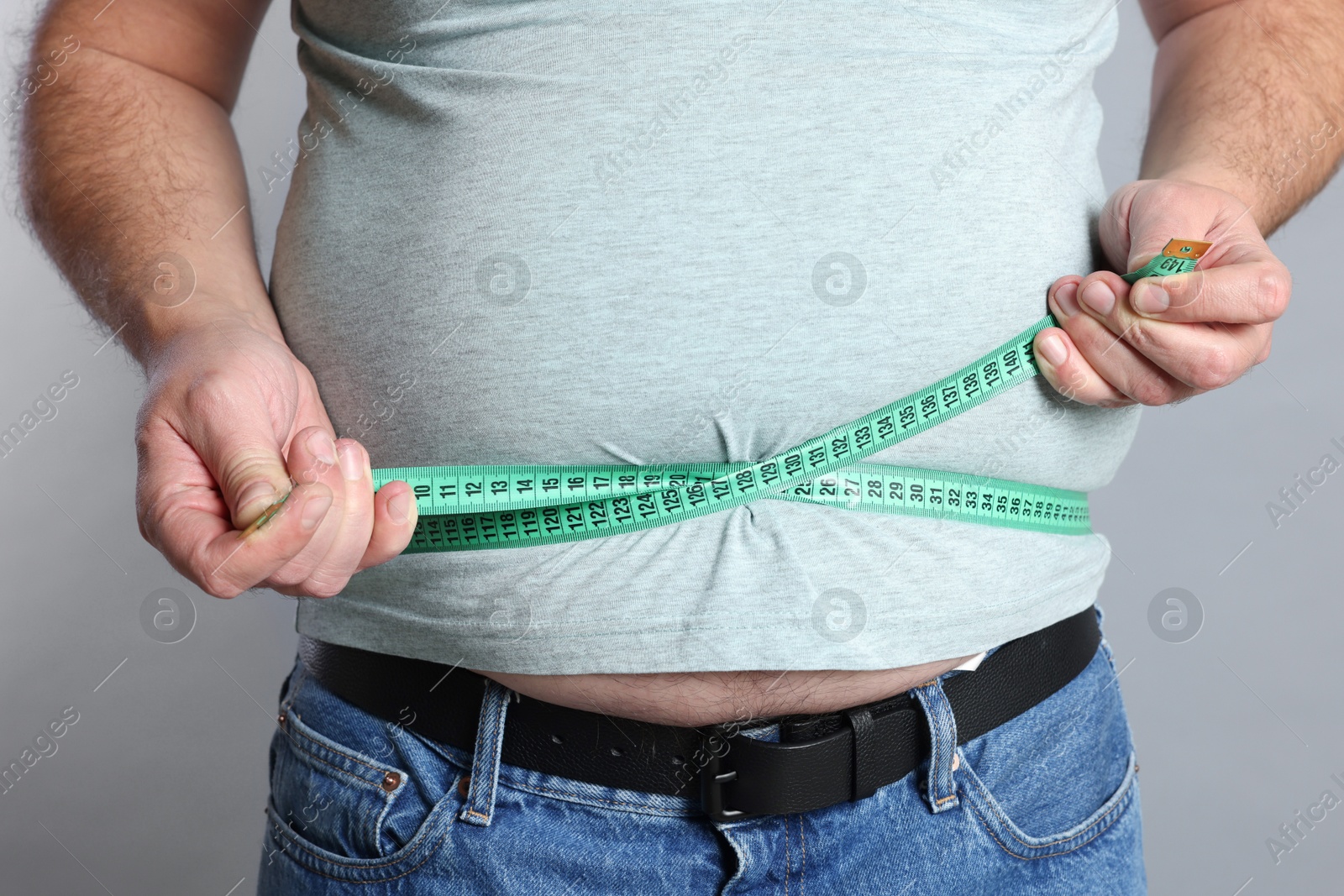 Photo of Overweight man measuring his belly with tape on grey background, closeup