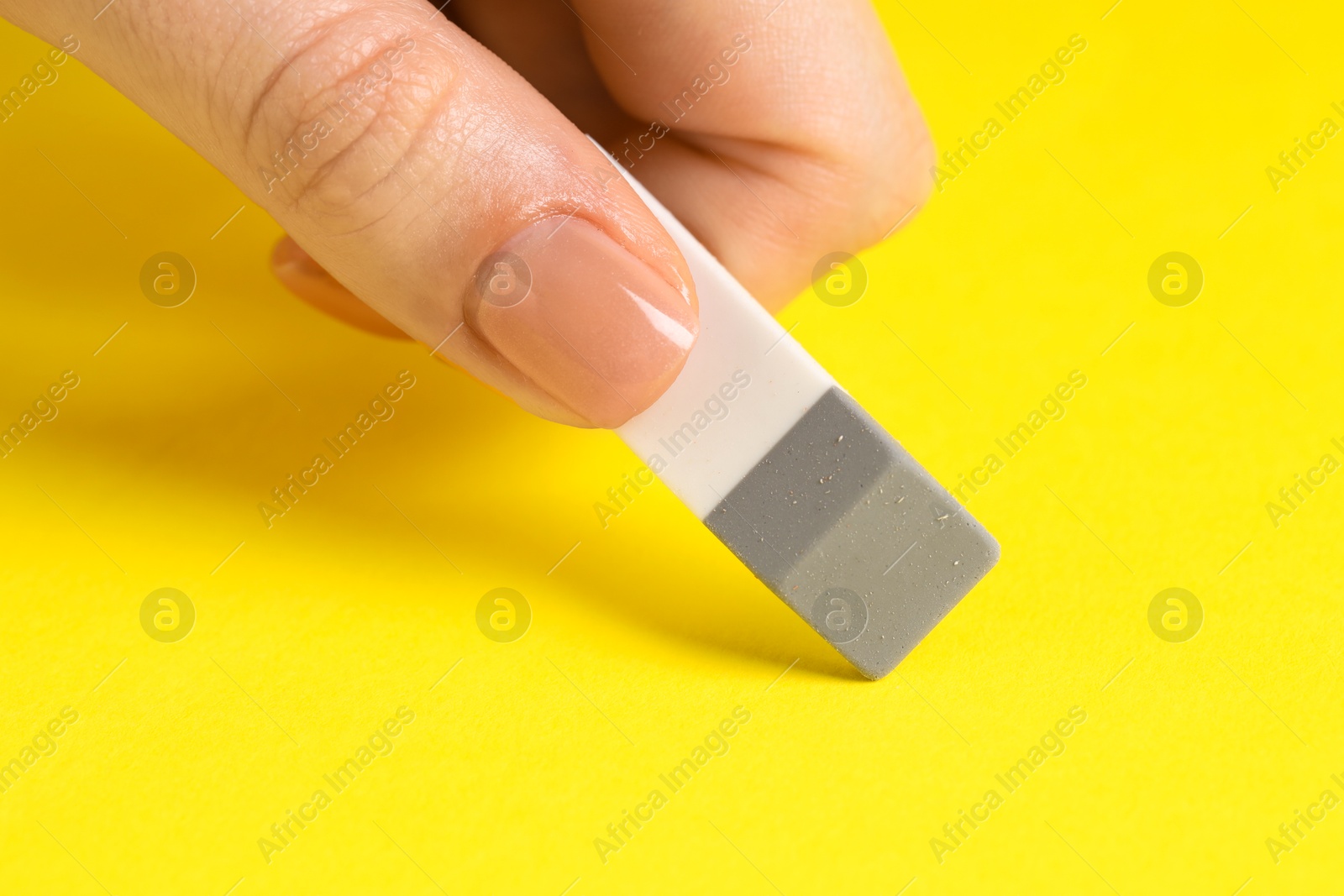 Photo of Woman using eraser on yellow background, closeup