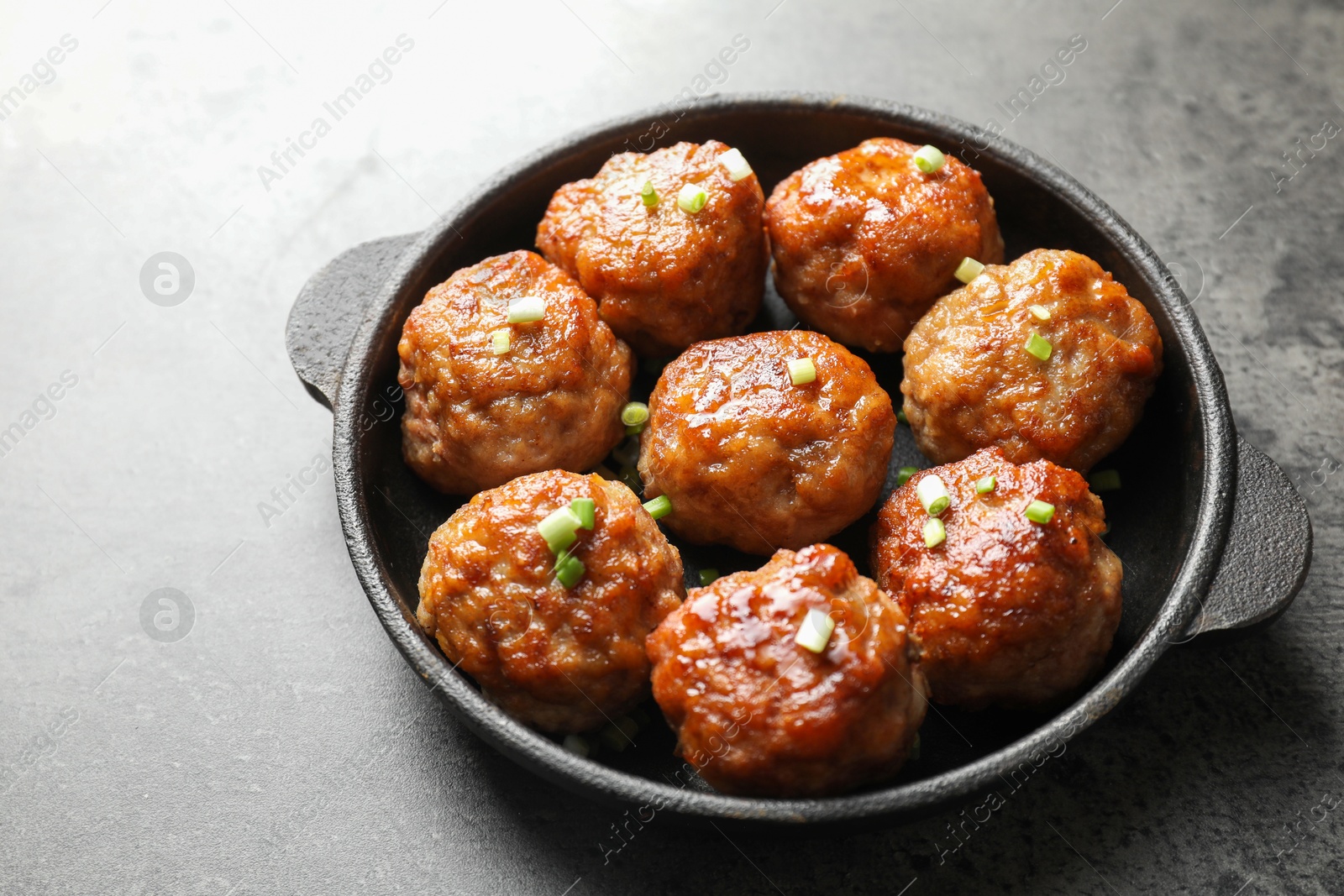 Photo of Tasty meatballs with green onion in baking dish on grey table, closeup