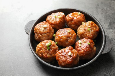 Photo of Tasty meatballs with green onion in baking dish on grey table, closeup