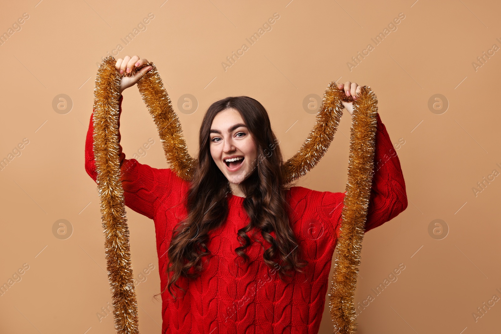 Photo of Happy young woman with tinsel on beige background