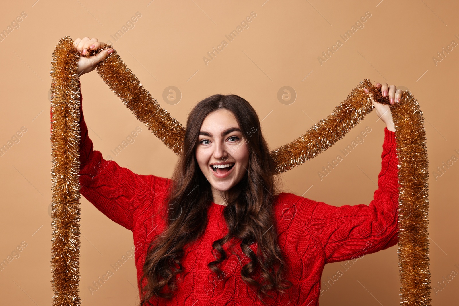 Photo of Happy young woman with tinsel on beige background