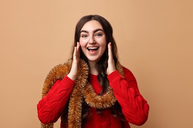 Photo of Happy young woman with tinsel on beige background