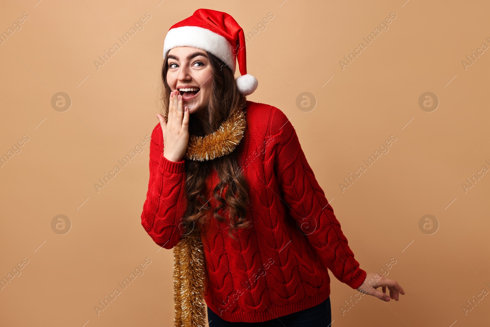 Photo of Happy young woman with tinsel and Santa hat on beige background